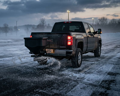 Rear of a black GMC Sierra with a Western Low Profile tailgate salt spreader on a snowy Wisconsin lot