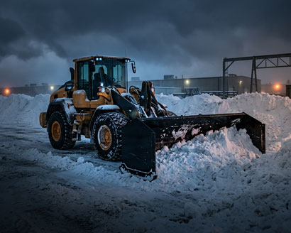Commercial wheel loader with a Western Pile Driver containment plow clearing a snow pile in an industrial lot